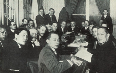 A group of about 20 men at the Congress of the Anti-Imperialism League in Brussels in 1927. The men sit around a table with papers and books, and Mohammad Hatta sits at the front.