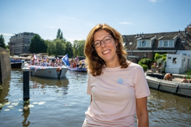 Sarah de Rijcke in een lichtroze T-shirt. Op de achtergrond vaart een boot van de Pride.